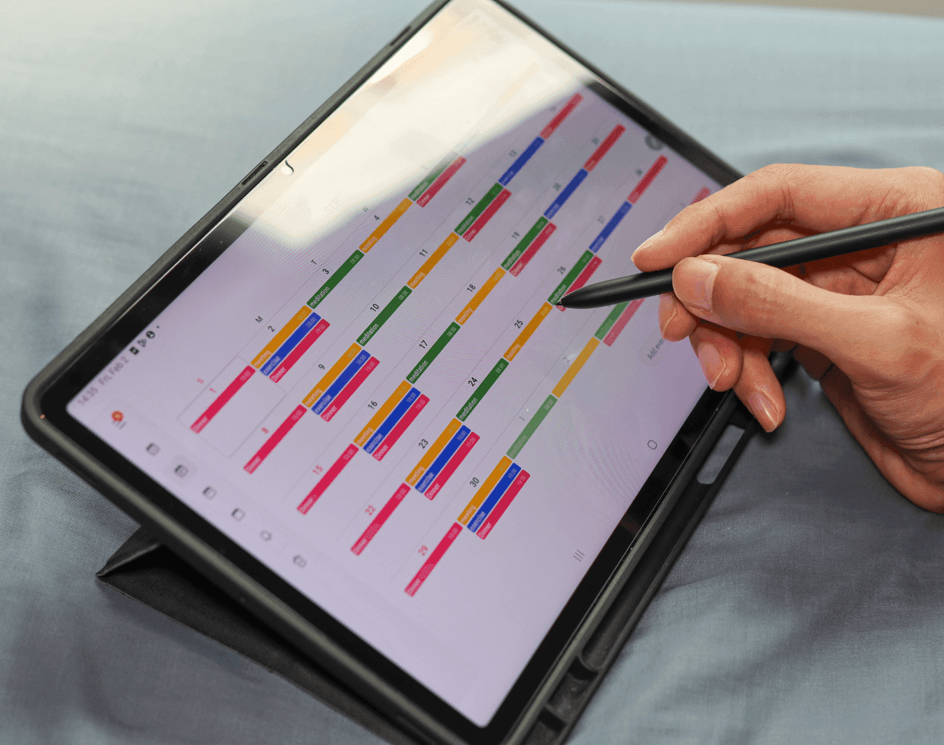 Hand using a stylus on a digital calendar displayed on a tablet, planning out a weekly content posting schedule.