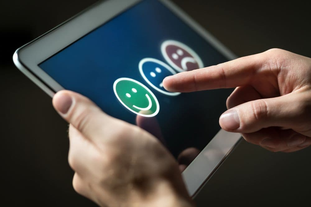 Person using a tablet and selecting a happy face emoji from a row of feedback icons, representing positive client interaction
