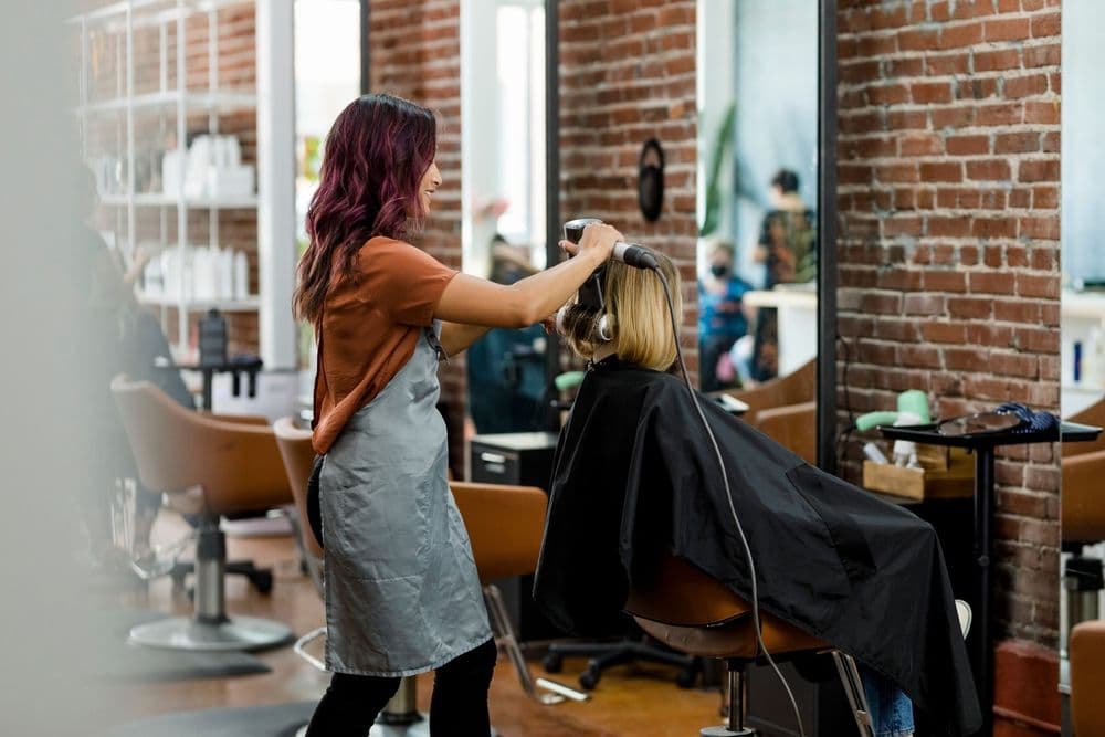 Hairstylist blow-drying a client’s hair in a modern salon, representing the conversion of online followers into real salon clients.