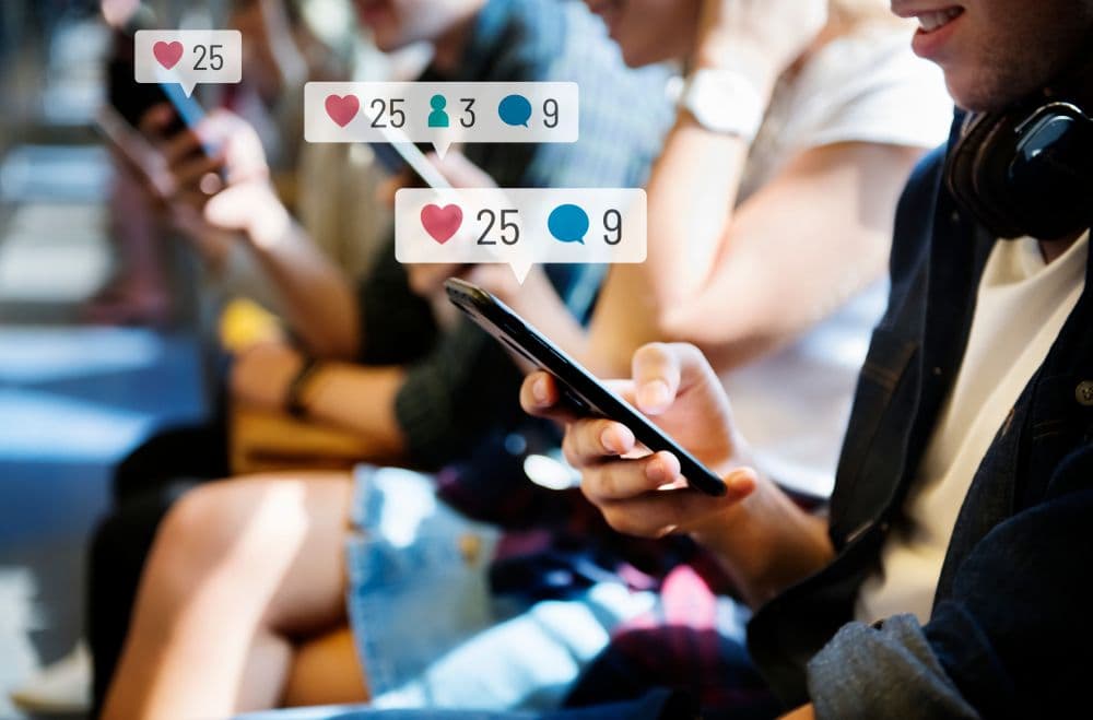 Close-up of people using smartphones with floating social media notifications showing likes, comments, and followers, representing online engagement metrics.