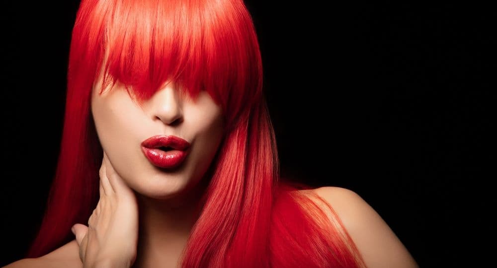 Fashion model with striking long red hair and bold red lips against a black background, symbolising attracting the right clients through standout social media presence.