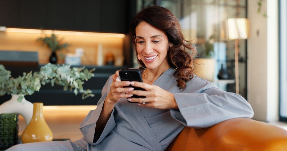 Smiling woman in a modern setting looking at her phone, representing positive engagement with shared and saved social media posts.